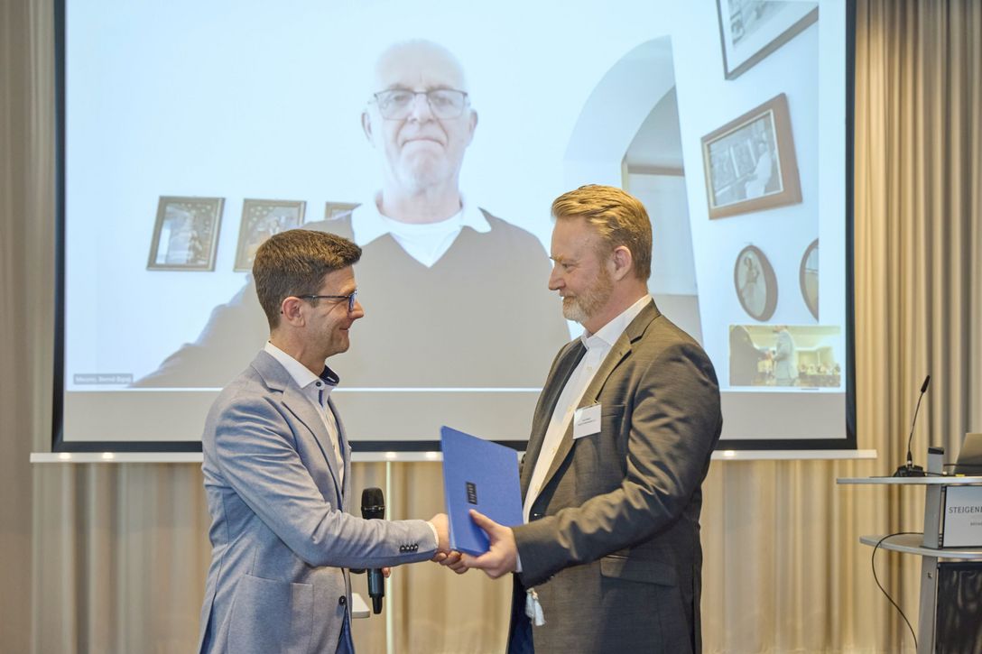 bpa-Hauptgeschäftsführer Norbert Grote gratuliert dem ehemaligen bpa-Landesvorsitzenden Sven Beyer und überreicht ihm im Namen von bpa-Präsidend Bernd  Meurer (im Hintergrund zugeschaltet) die goldene Ehrennadel samt Urkunde